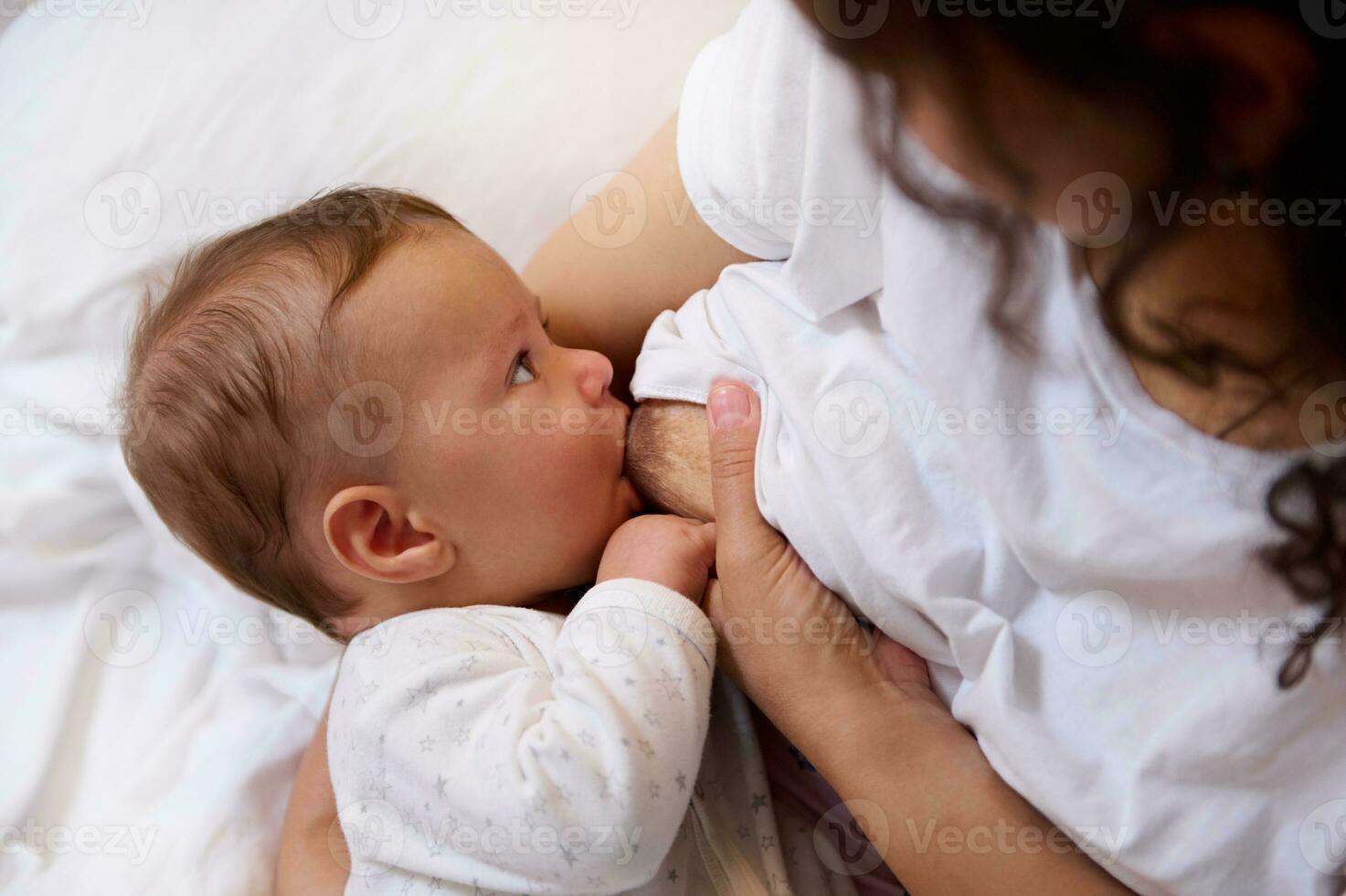 de cerca retrato adorable bebé chico vestido en blanco ropa, mamón el sano Leche desde el pecho de su madre foto