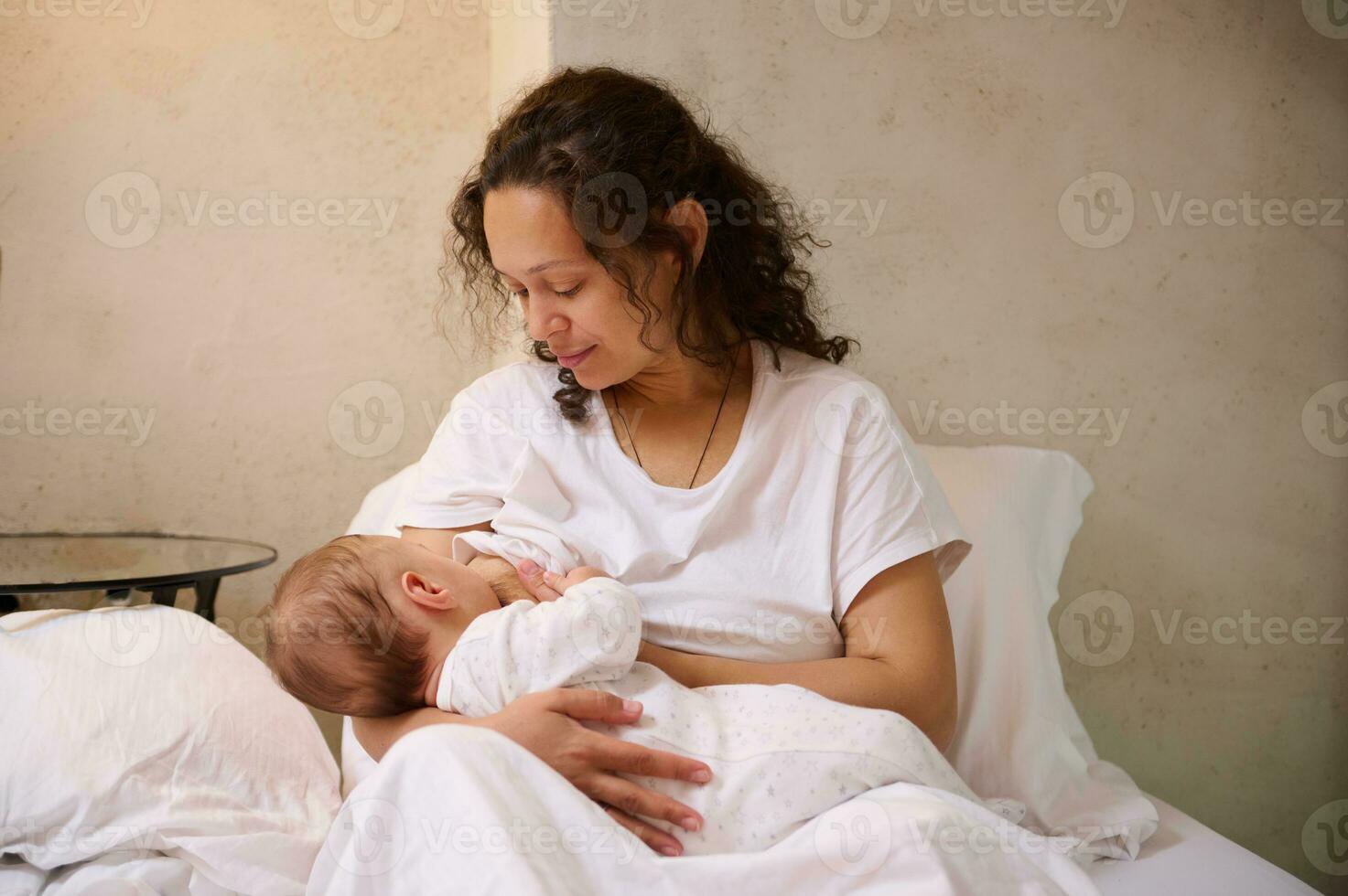 Newborn baby boy sucking milk from mothers breast. Confident portrait of a beautiful woman, young loving mom while breastfeeding baby in cozy home interior. Pregnancy and maternity leave lifestyle photo