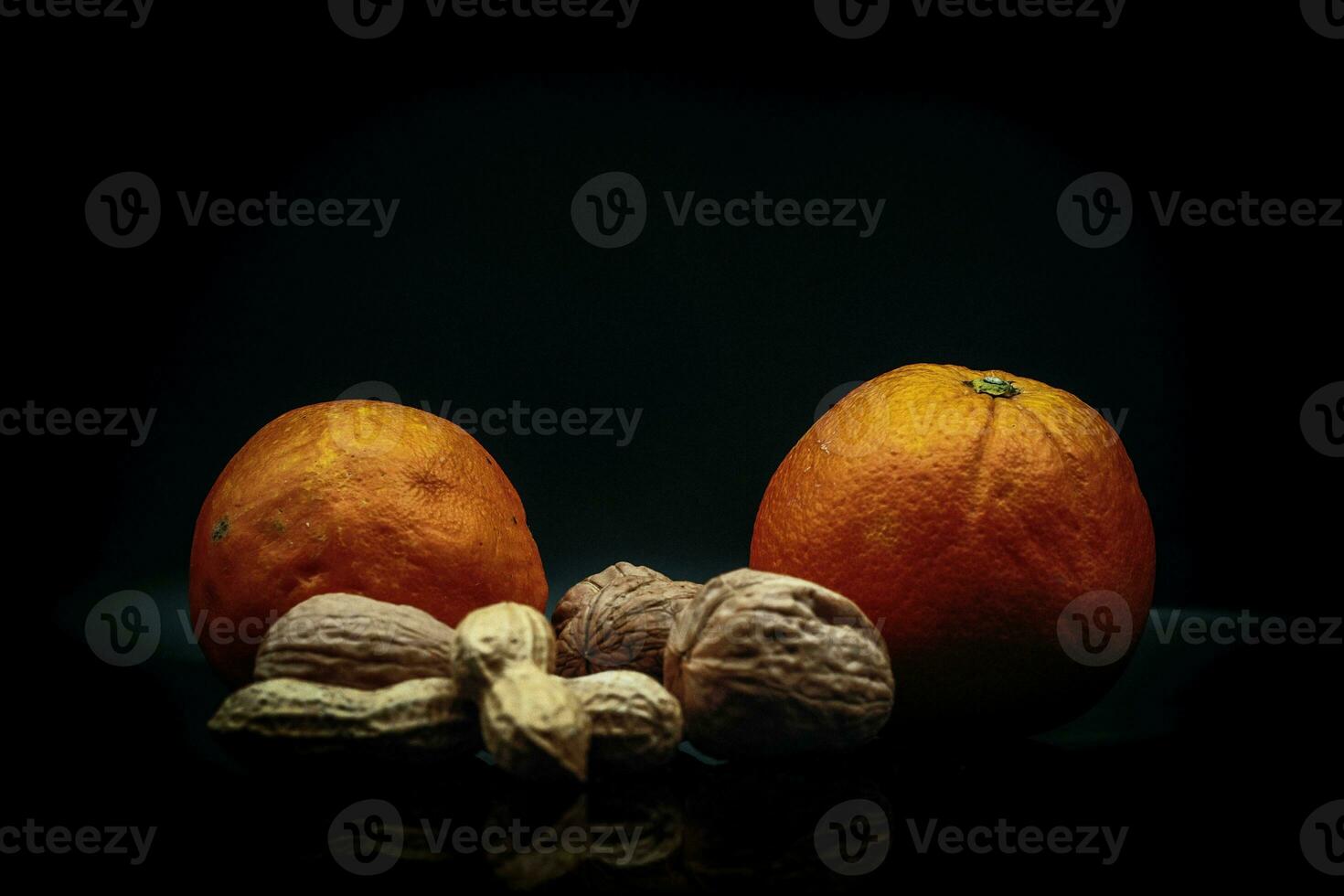 studio photo on black background of fresh and dried fruit. oranges, peanuts and walnuts in an Italian study