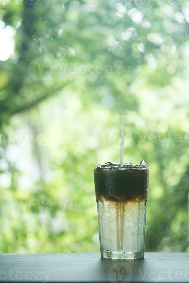 Iced americano in glass, showing two layers of black coffee and water against nature background photo