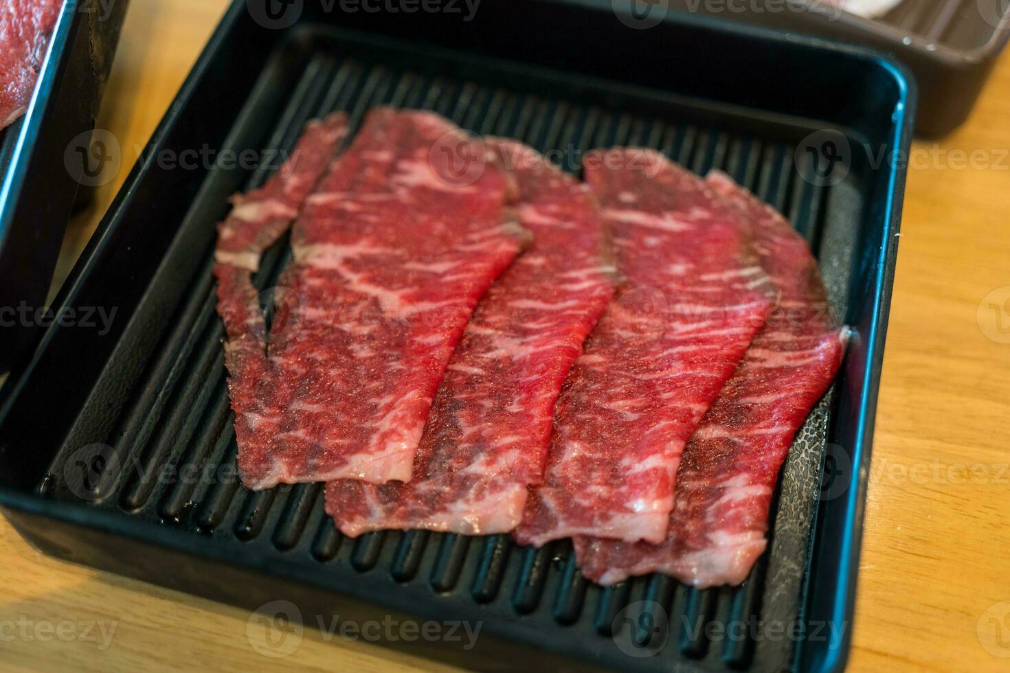 Premium thinly sliced beef in black tray on wood table photo