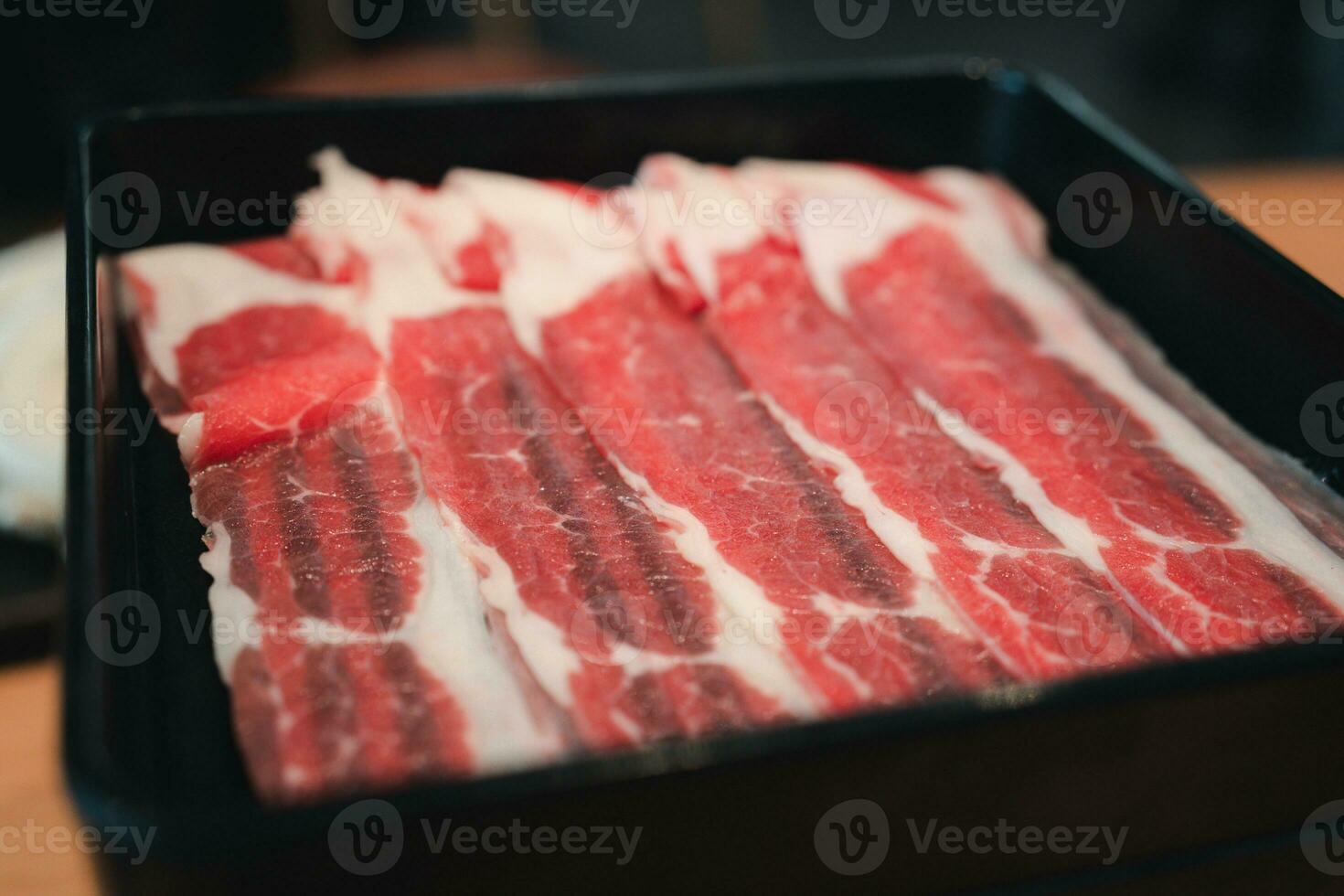 Thin beef slices for of raw thinly sliced beef served on black tray photo