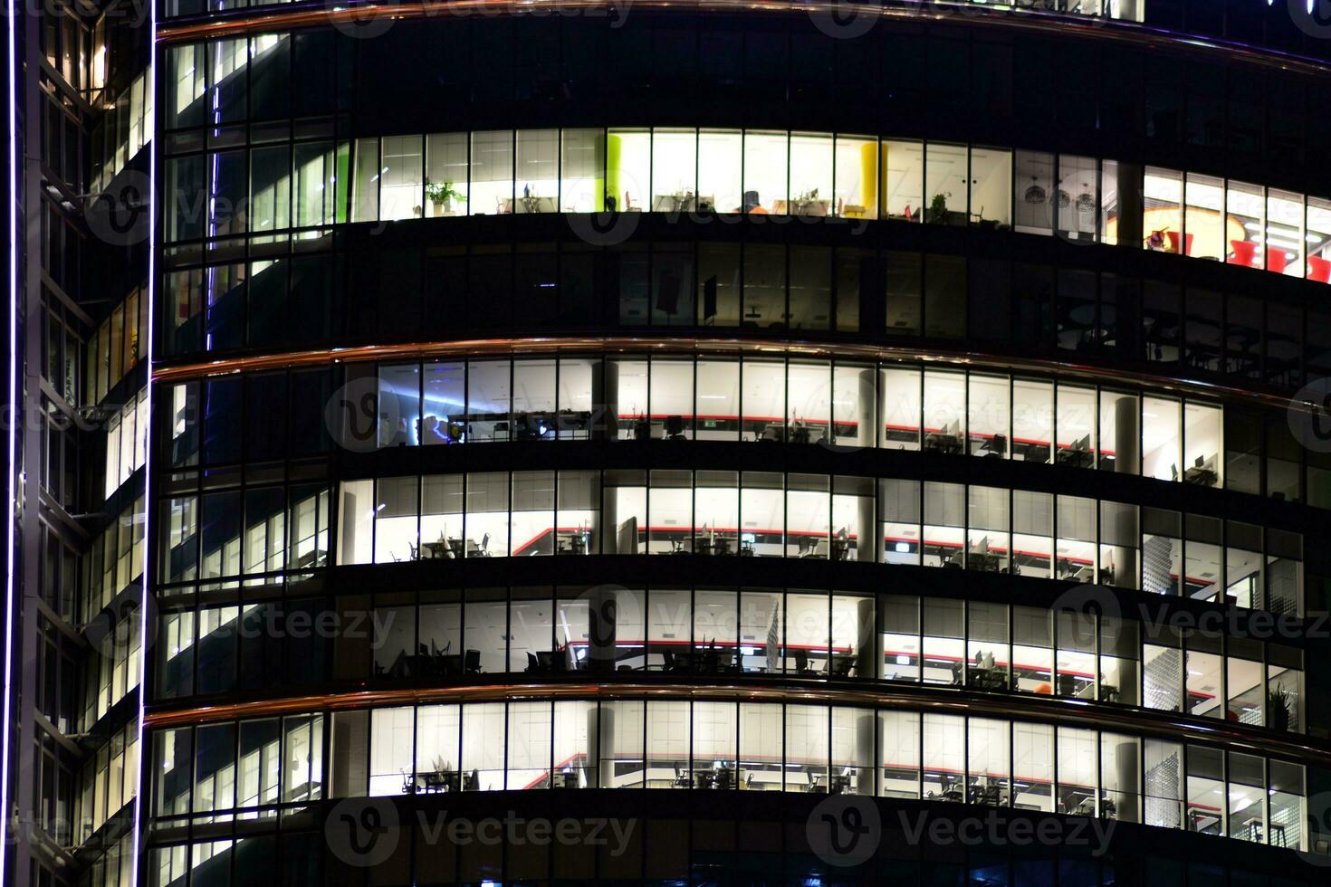 Fragment of the glass facade of a modern corporate building at night. Modern glass office  in city. Big glowing windows in modern office buildings at night, in rows of windows light shines. photo