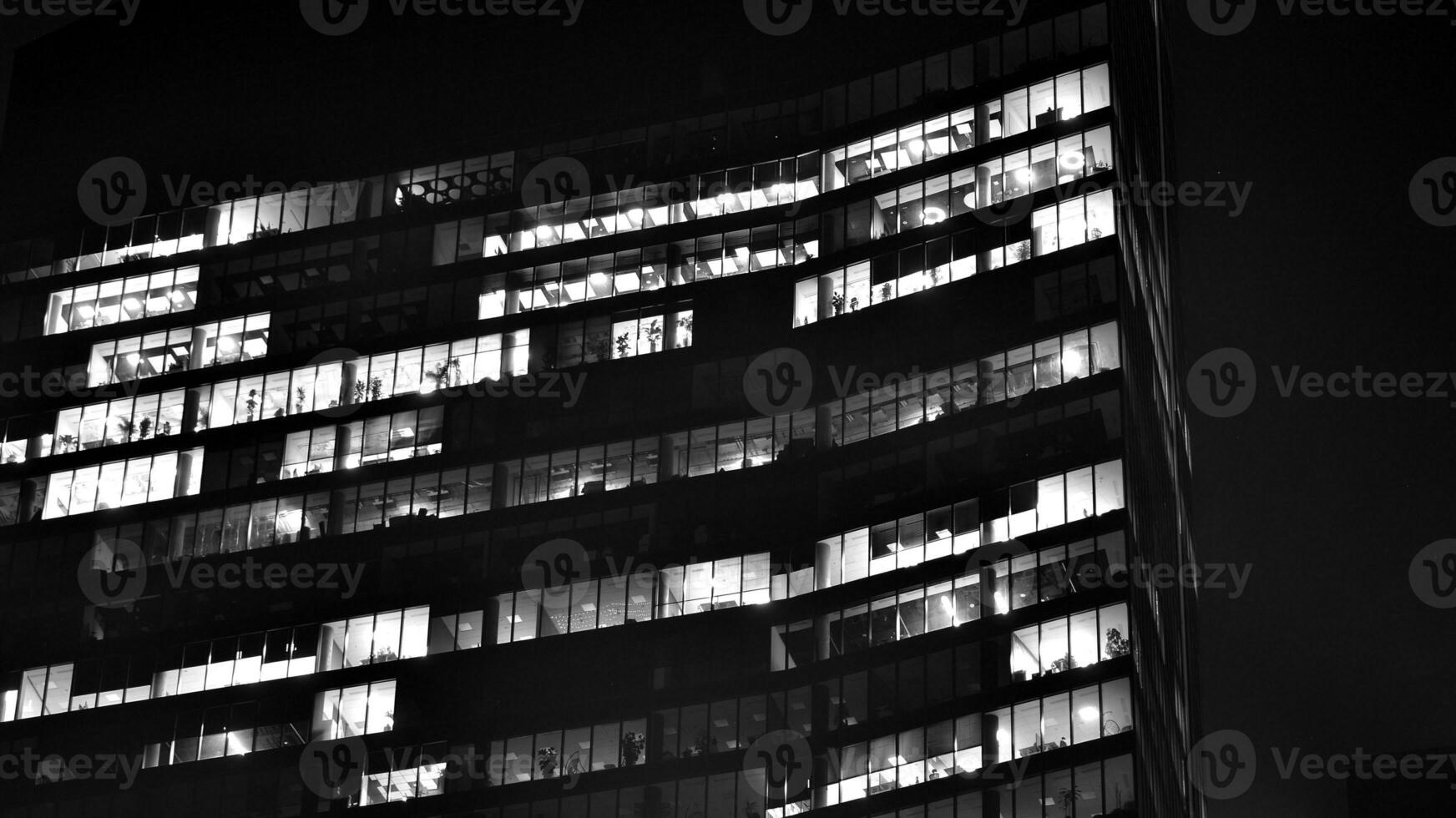 Pattern of office buildings windows illuminated at night. Glass architecture ,corporate building at night - business concept. Black and white. photo