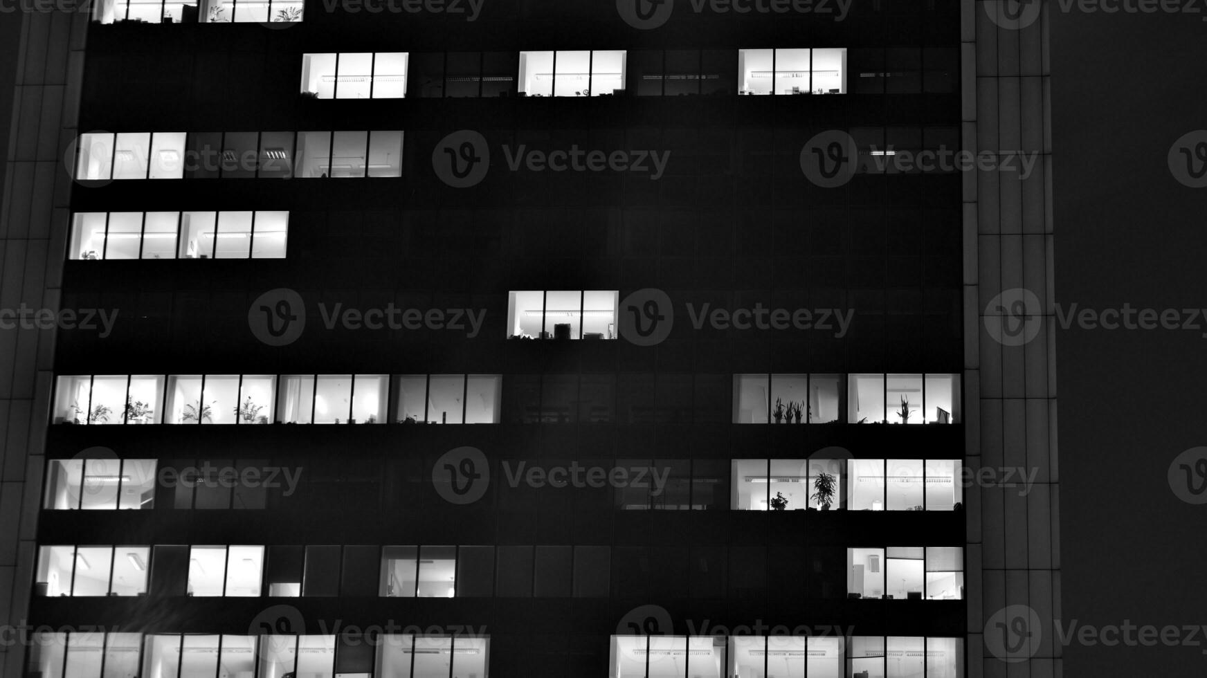 Pattern of office buildings windows illuminated at night. Glass architecture ,corporate building at night - business concept. Black and white. photo