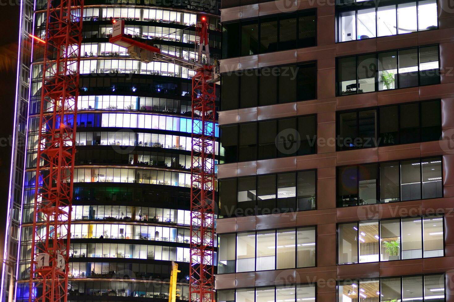 Fragment of the glass facade of a modern corporate building at night. Modern glass office  in city. Big glowing windows in modern office buildings at night, in rows of windows light shines. photo