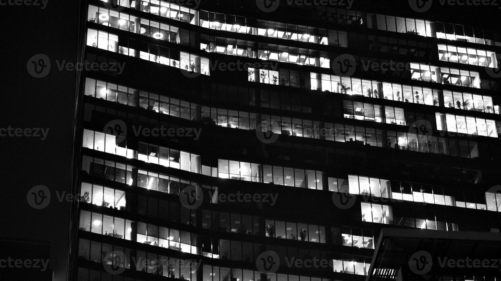 Pattern of office buildings windows illuminated at night. Glass architecture ,corporate building at night - business concept. Black and white. photo