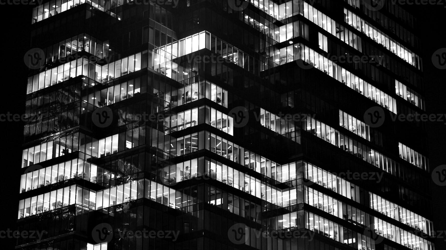 Pattern of office buildings windows illuminated at night. Glass architecture ,corporate building at night - business concept. Black and white. photo