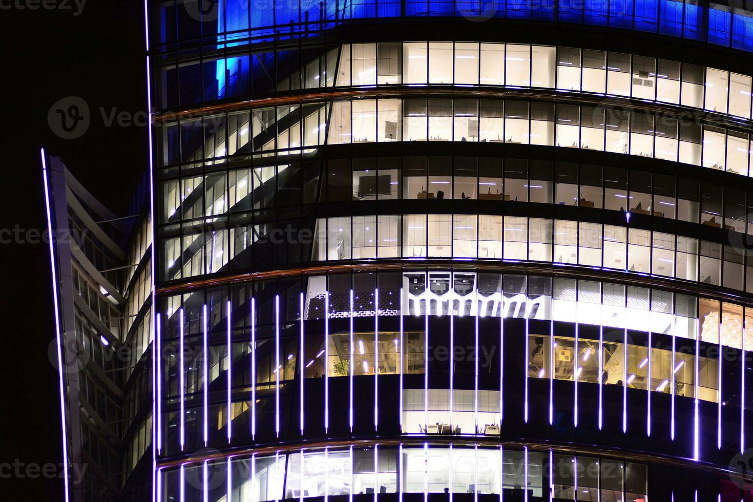 Fragment of the glass facade of a modern corporate building at night. Modern glass office  in city. Big glowing windows in modern office buildings at night, in rows of windows light shines. photo