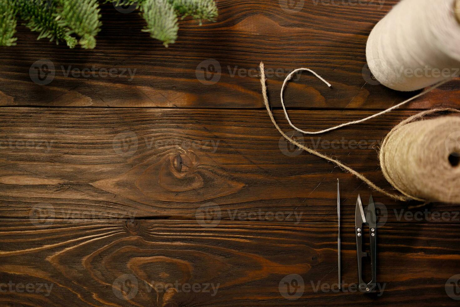 Crochet hook, scissors, twisted cotton rope and burlap cord on wooden table decorated with spruce branches photo