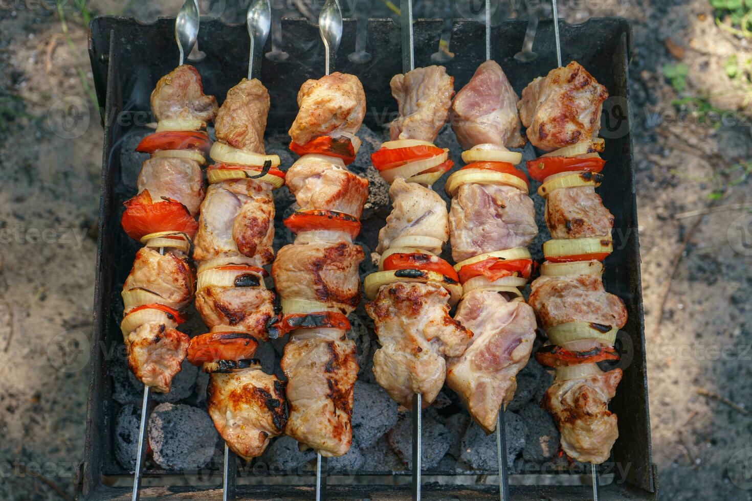 Grilled pieces of meat on skewers, shish kebab with vegetables, cooking process on brazier photo