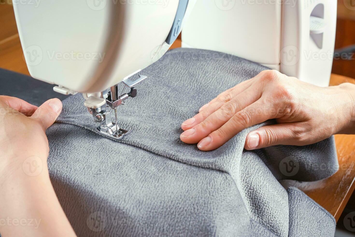 Female hands stitching gray fabric on modern sewing machine. Close up view of sewing process. photo