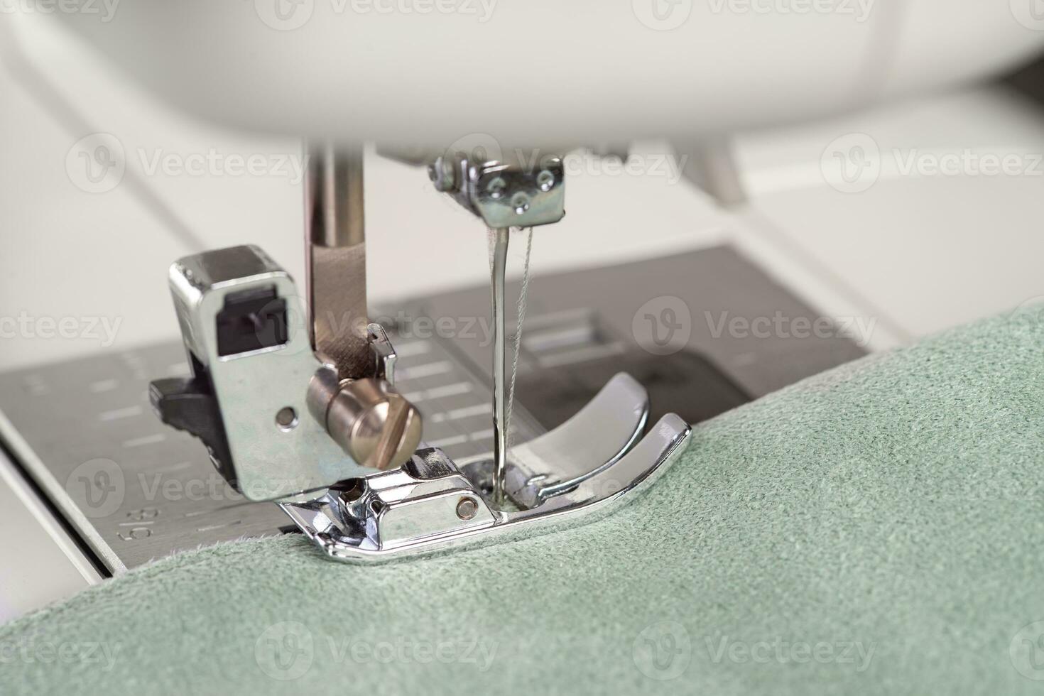 Modern sewing machine presser foot with green fabric and thread, closeup, macro photo