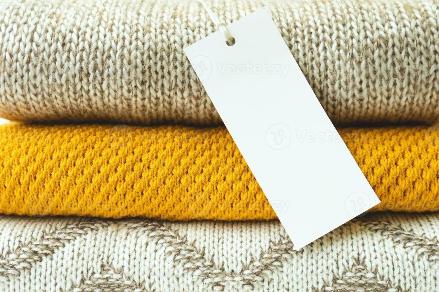 White blank rectangular clothing tag on stack of knitted clothes background close up photo