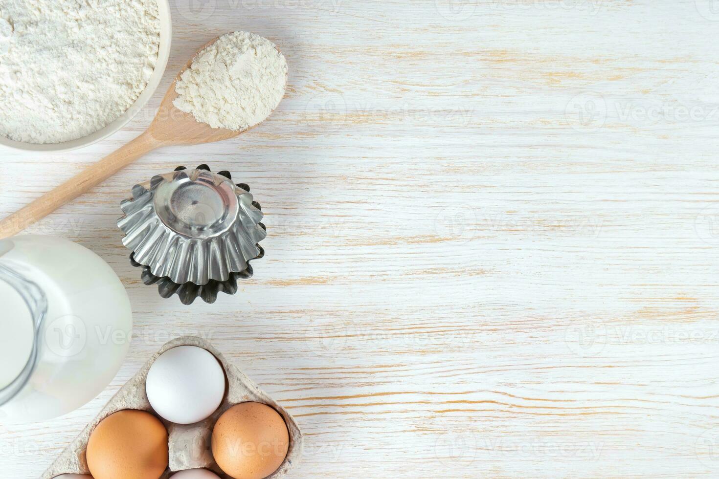 Baking ingredients flour, eggs, milk, bakeware on white wooden background with copy space photo