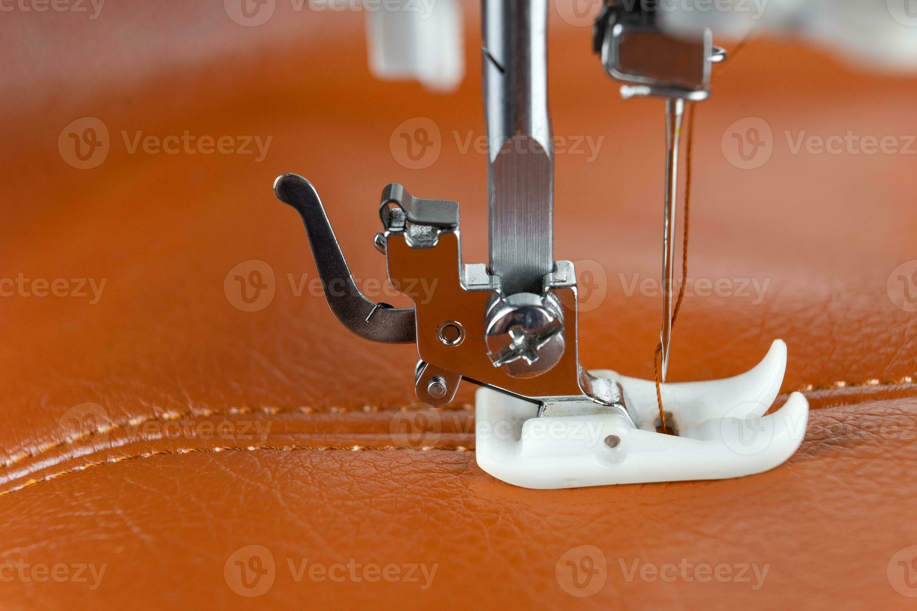 Modern sewing machine presser foot with a needle sews brown leather