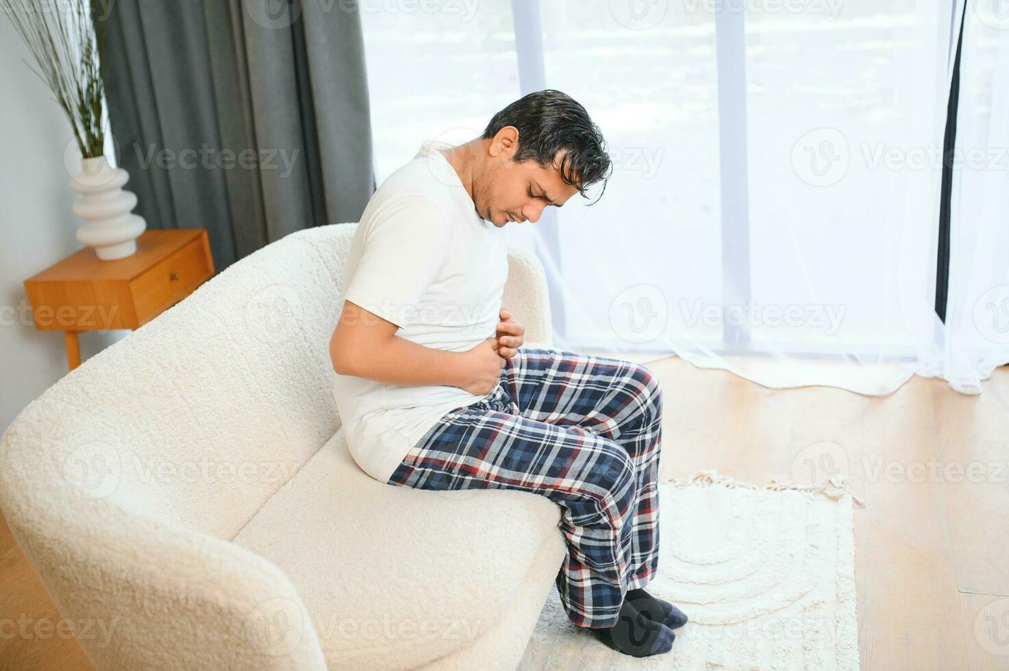 Sad exhausted guy of indian and arabian ethnicity, holds his hands on his stomach, grimaces from pain in his stomach, suffers from poisoning, spasm, stomach problems photo