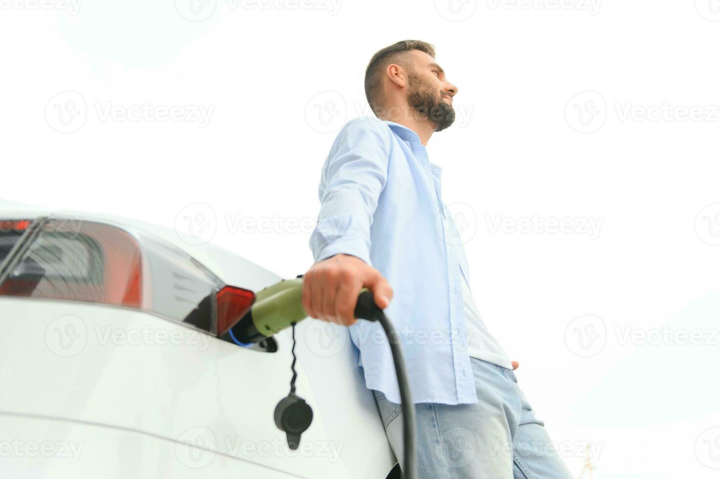 hombre participación poder cargando cable para eléctrico coche en al aire libre coche parque. y él s yendo a conectar el coche a el cargando estación en el estacionamiento lote cerca el compras centro. foto