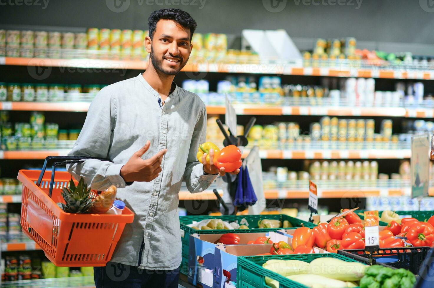 Closeup portrait, handsome young man picking up bell peppers, choosing yellow and orange vegetables in grocery store photo