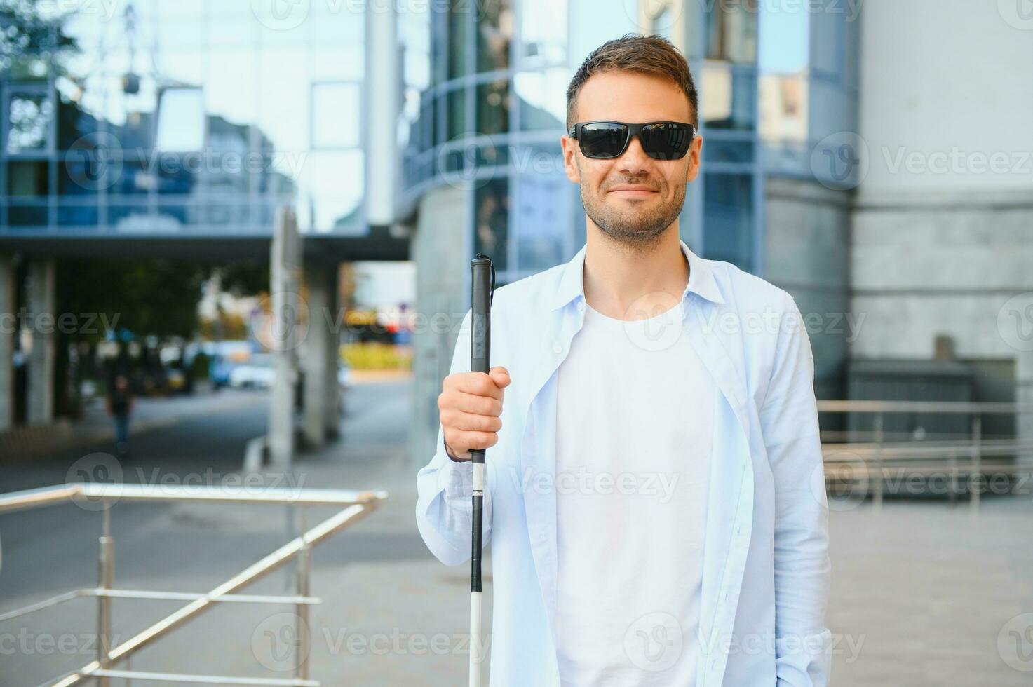 Young handsome blinded man walking with stick in town photo