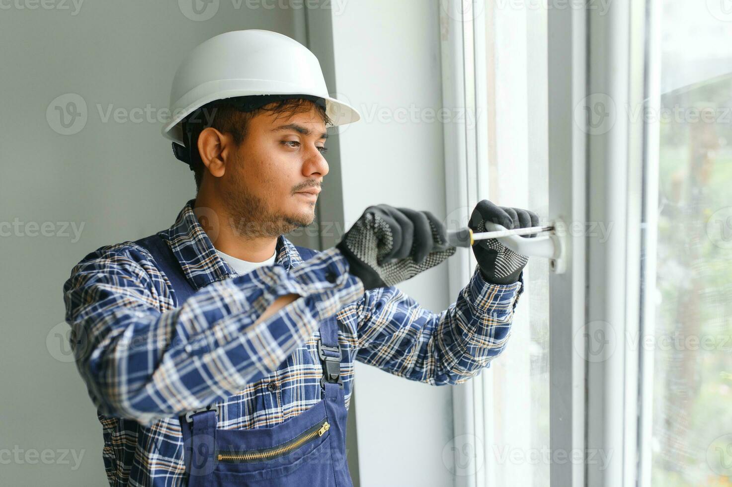 Indian Workman in overalls installing or adjusting plastic windows in the living room at home photo