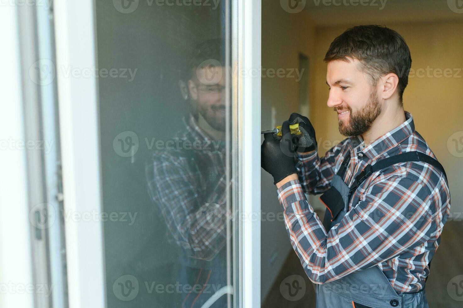 Workman in overalls installing or adjusting plastic windows in the living room at home photo