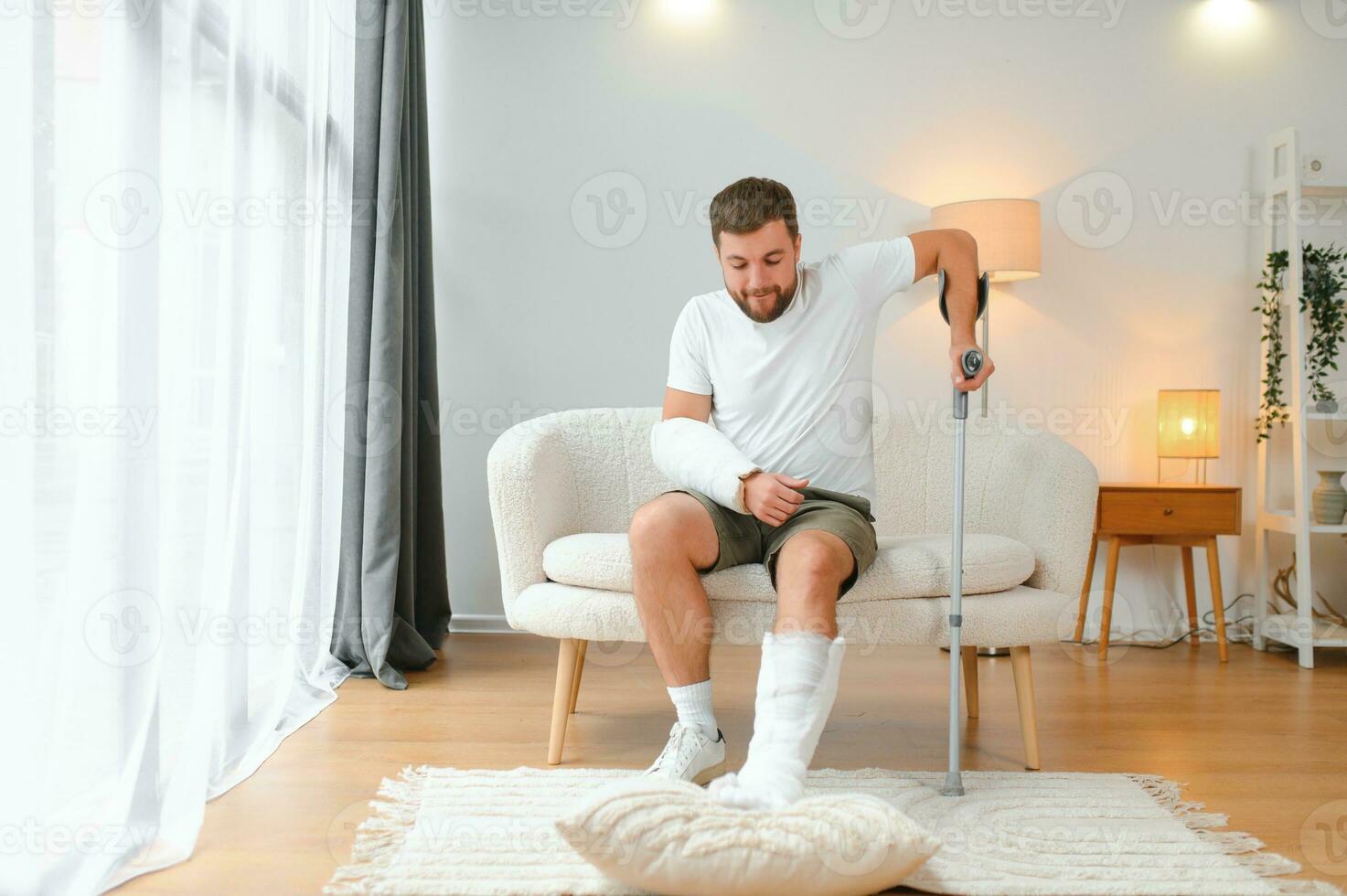 man recovery from accident fracture broken bone injury with leg splints in cast neck splints collar arm splints sling support arm in living room. Social security and health insurance concept photo