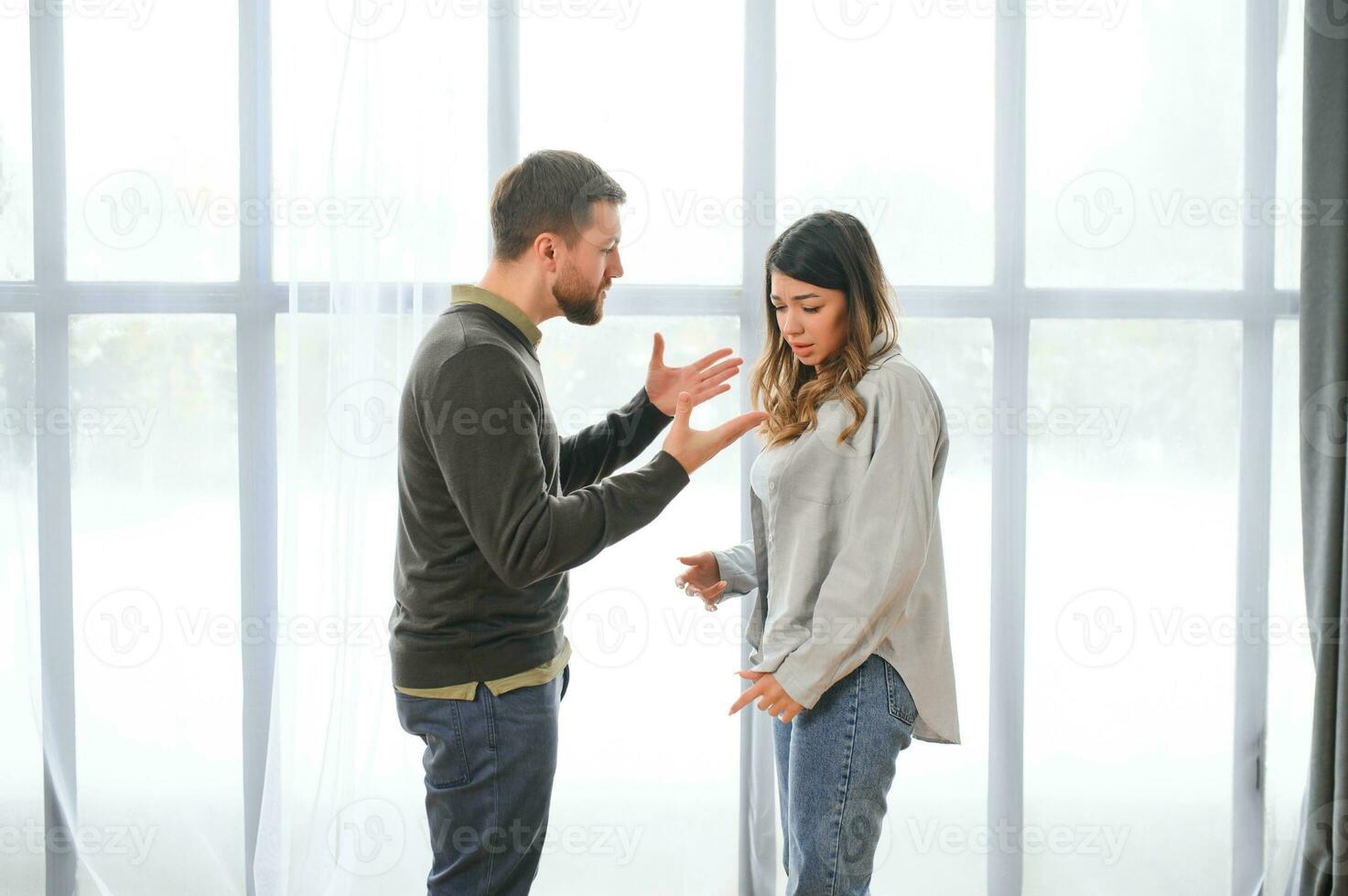Emotional man gesturing and shouting at his wife, young couple having quarrel at home. Domestic abuse concept photo