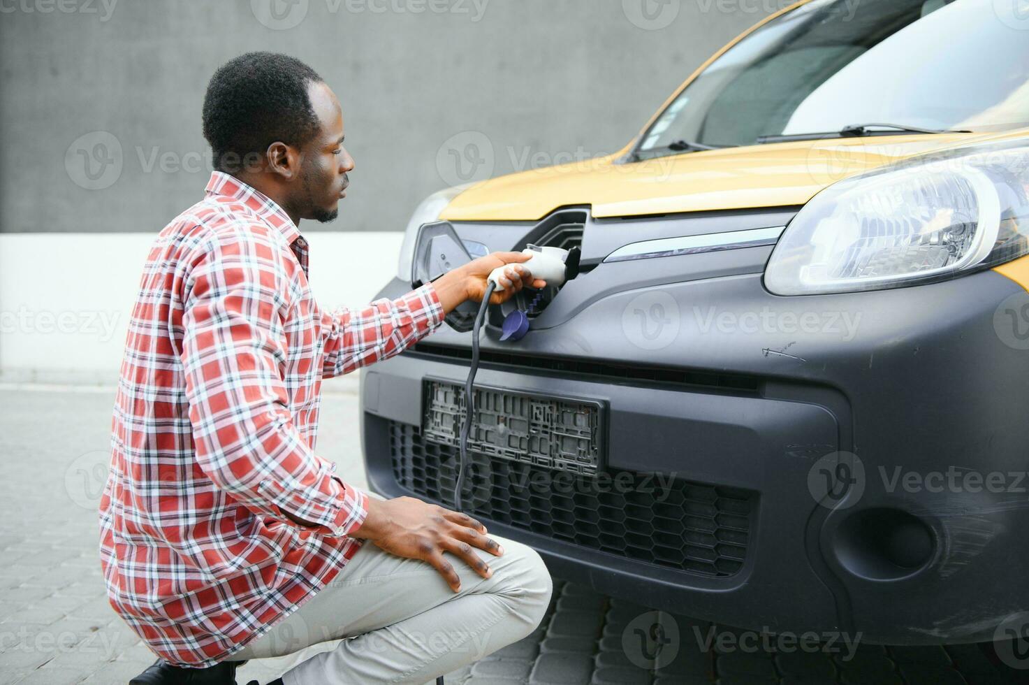 Stylish man inserts the charging cable into the socket of electric car photo
