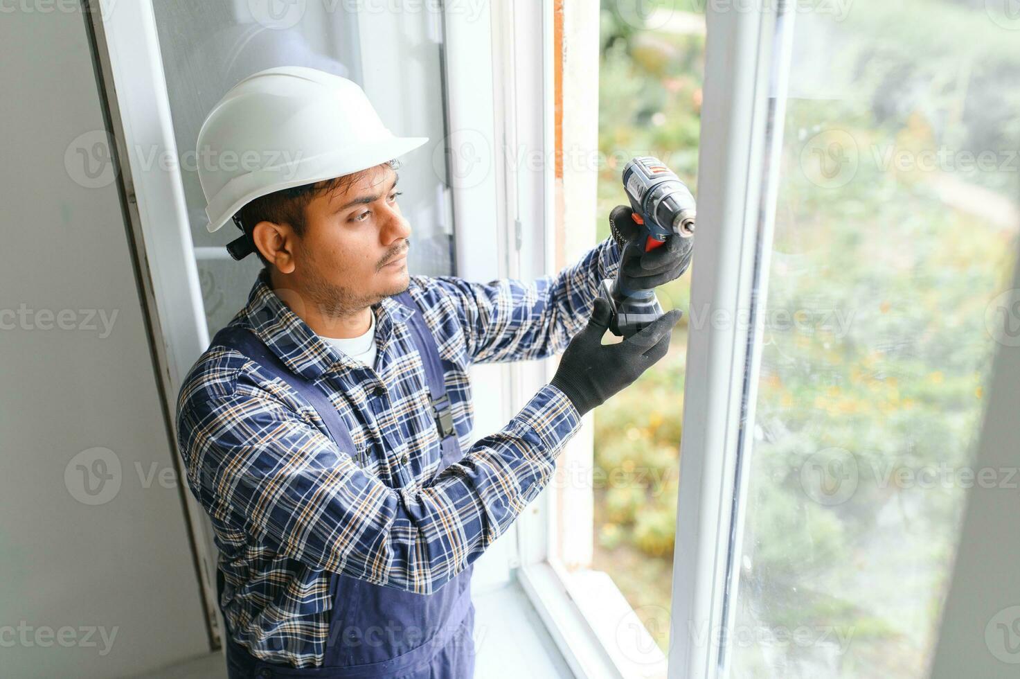 Indian Workman in overalls installing or adjusting plastic windows in the living room at home photo