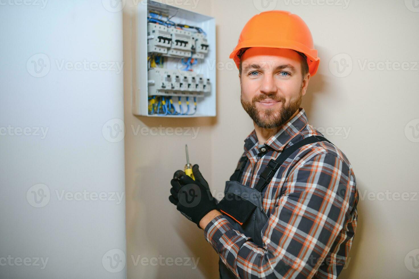 un masculino electricista trabajos en un tablero de conmutadores con un eléctrico conectando cable foto