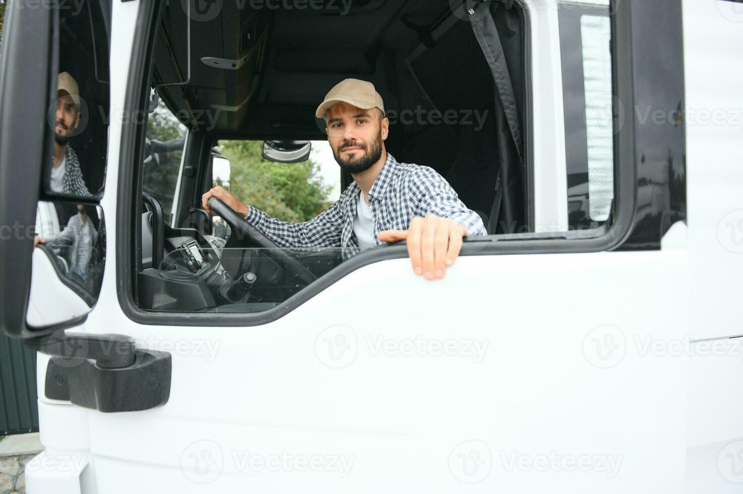 A driver sitting inside the semi-truck while looking through the open window with multiple trucks parked in the background photo