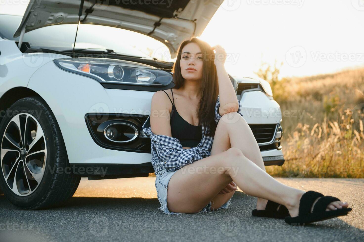 Beautiful young girl sitting at a broken car on the road desperate to get help photo
