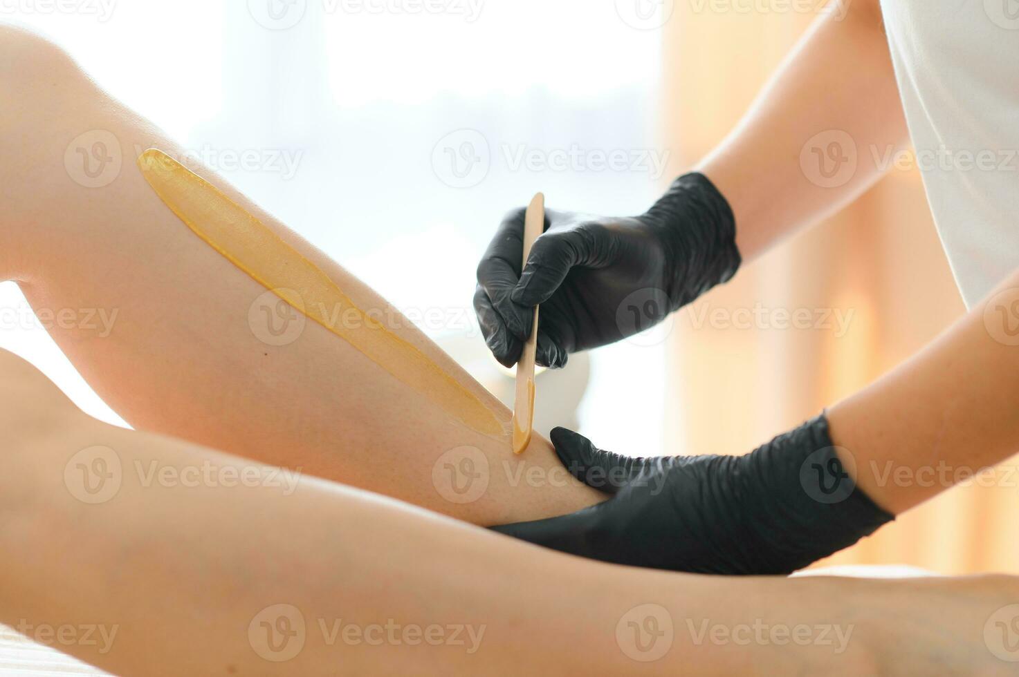 Young woman depilating legs with liquid sugar in spa center photo