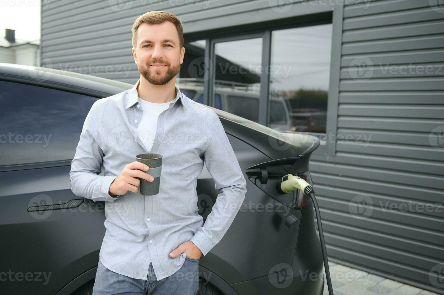 hermoso hombre Bebiendo café mientras cargando eléctrico coche foto