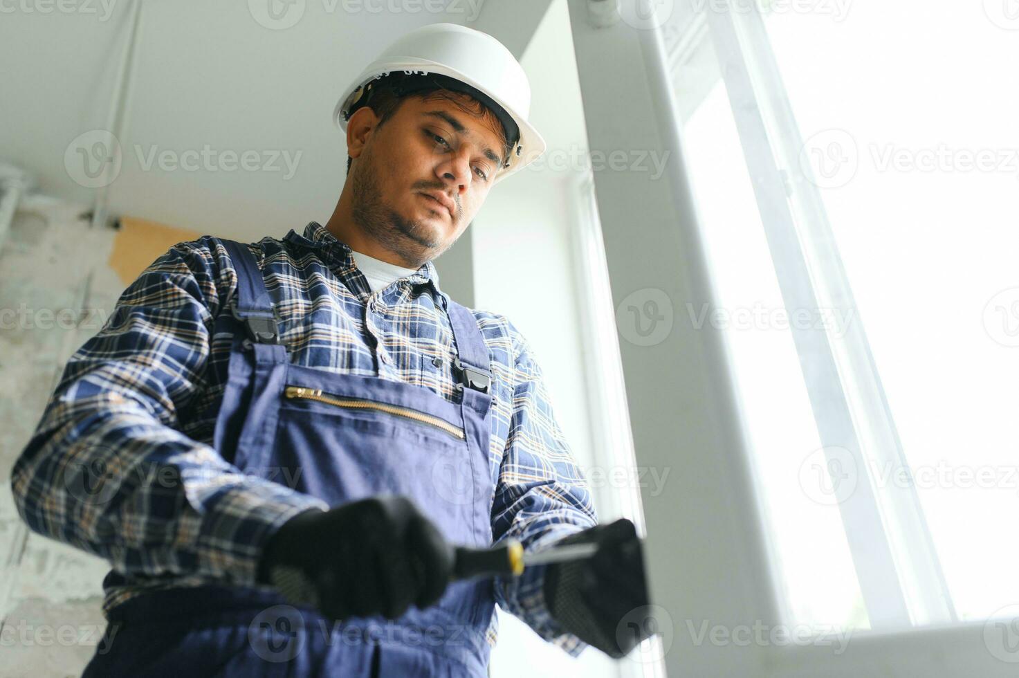 Indian Workman in overalls installing or adjusting plastic windows in the living room at home photo