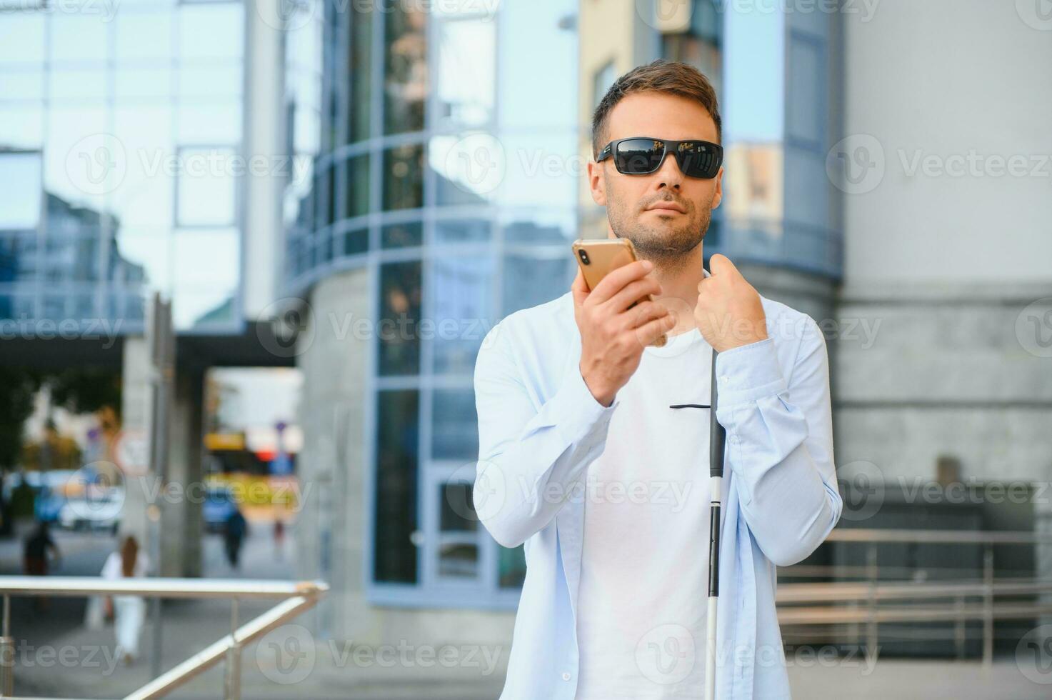 Young blind man with smartphone in city, calling photo