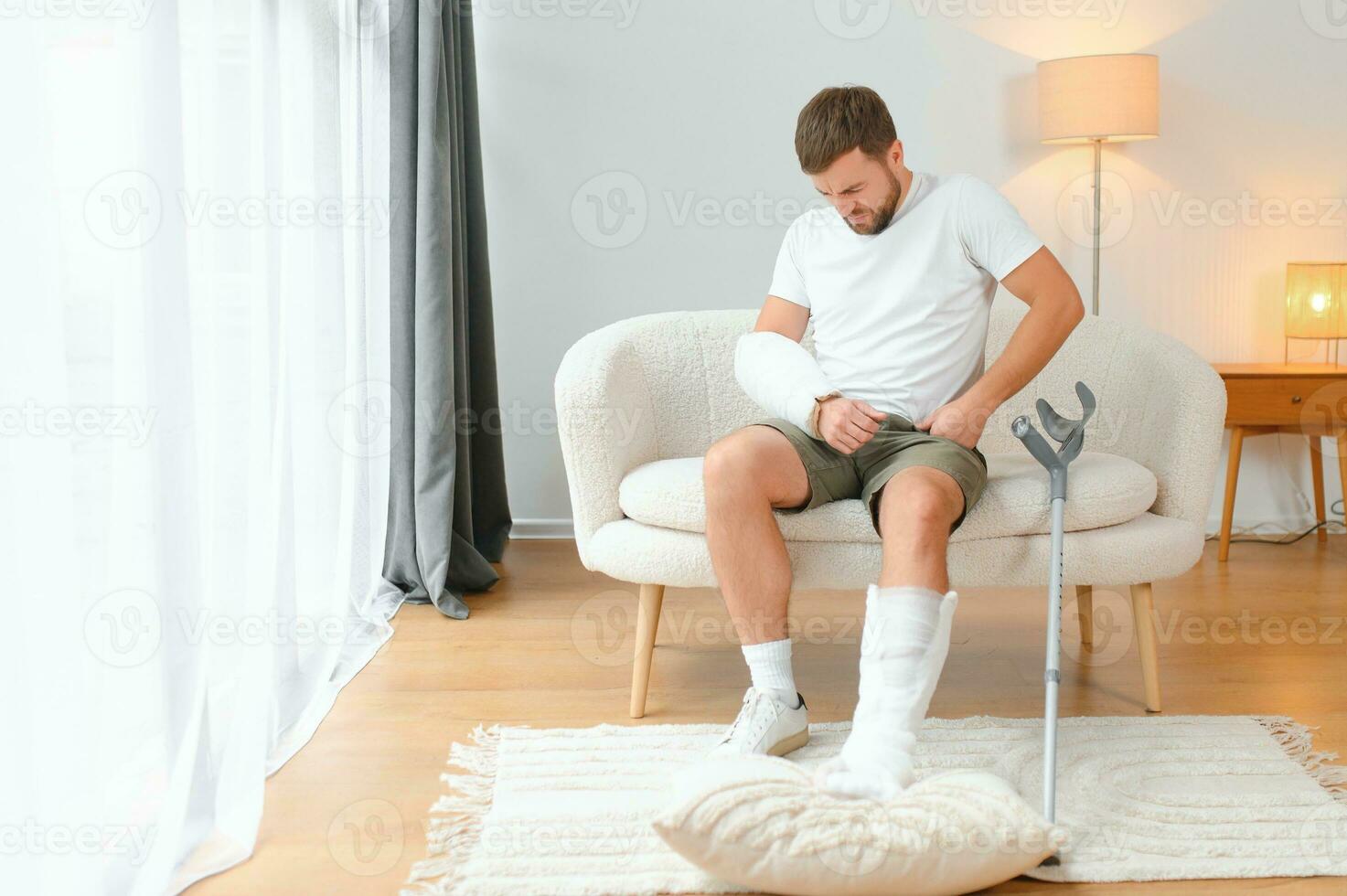 man recovery from accident fracture broken bone injury with leg splints in cast neck splints collar arm splints sling support arm in living room. Social security and health insurance concept photo