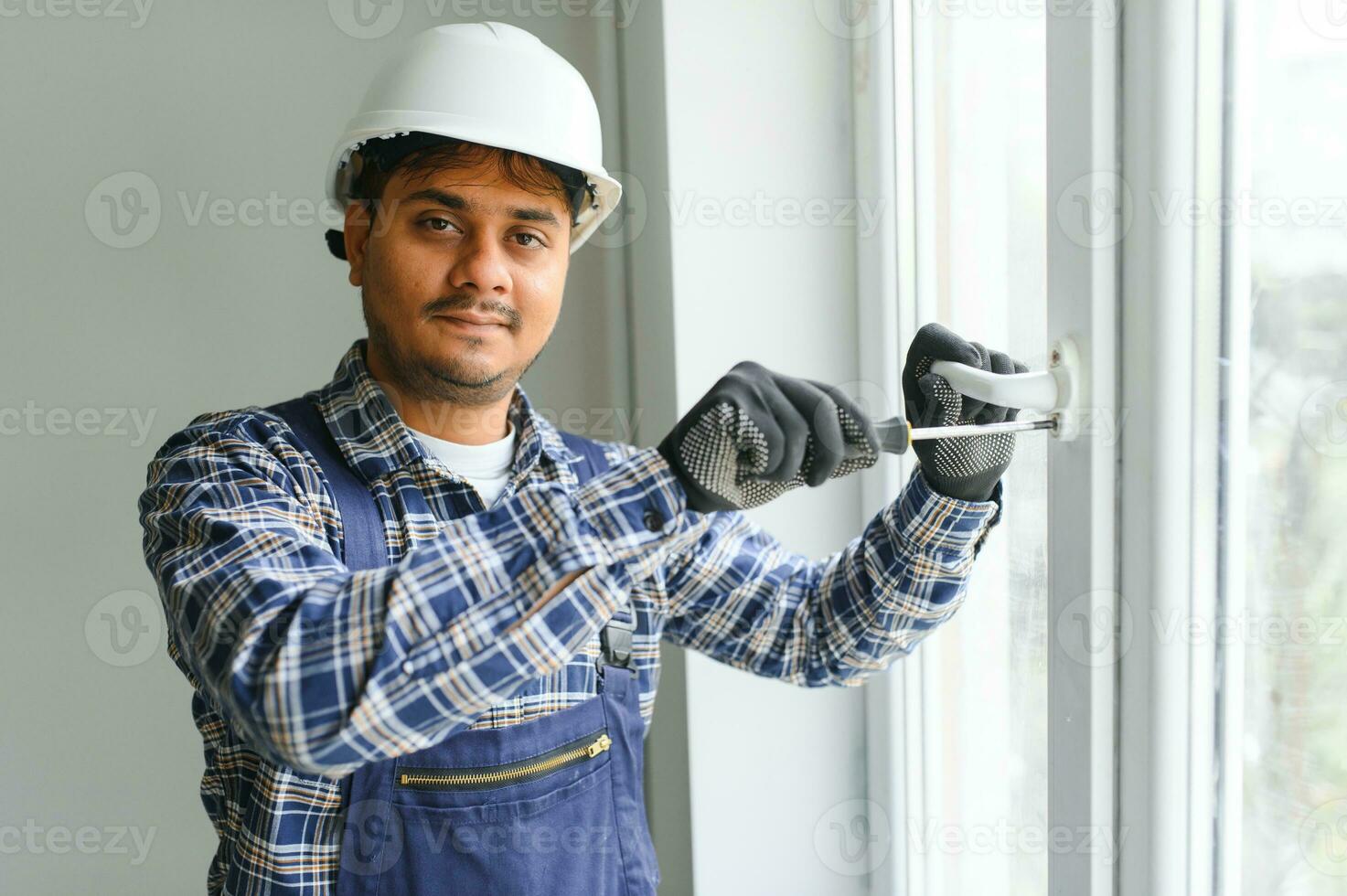 Indian Workman in overalls installing or adjusting plastic windows in the living room at home photo