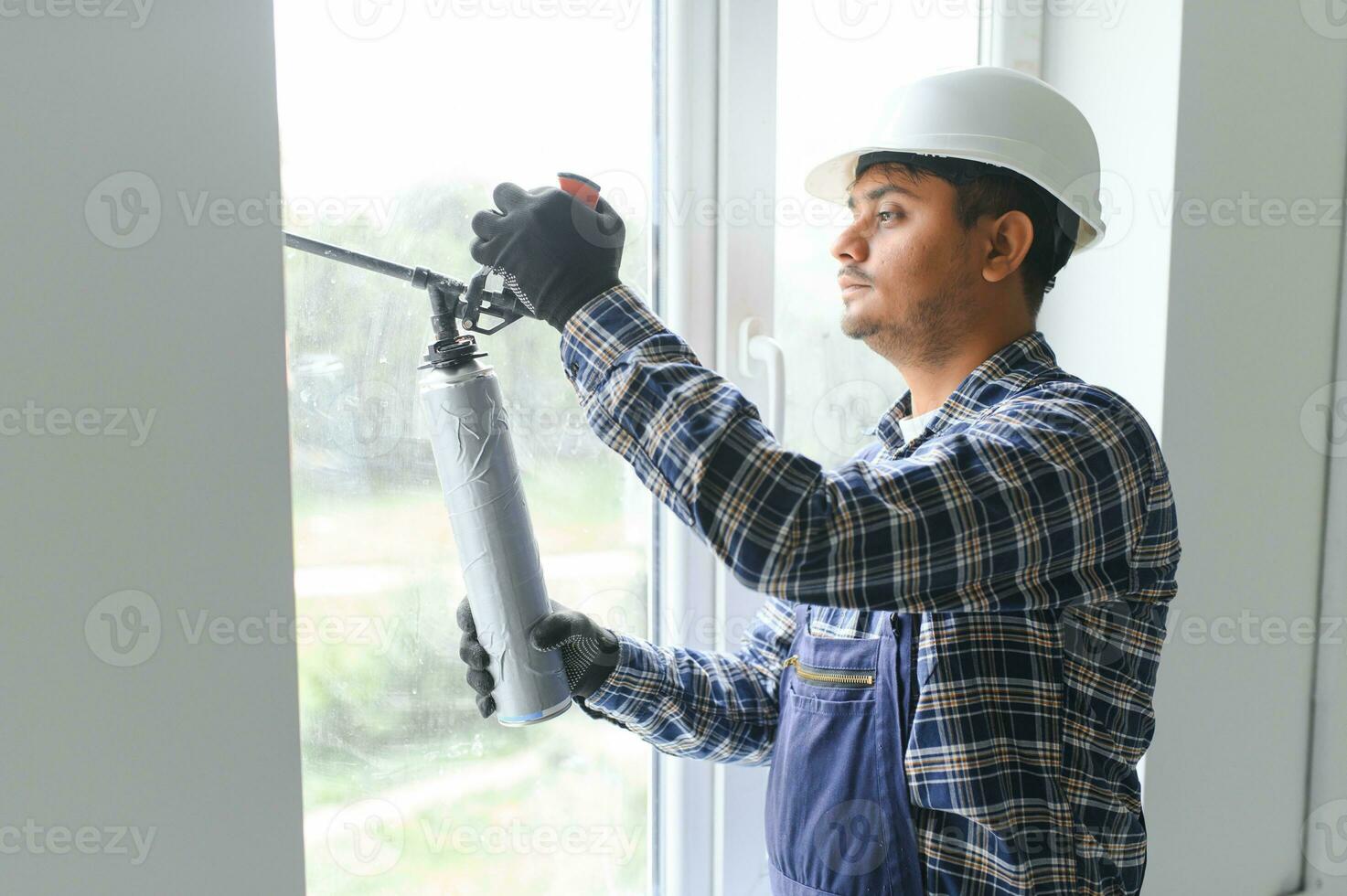 indio trabajador utilizando un silicona tubo para reparando de ventana interior foto