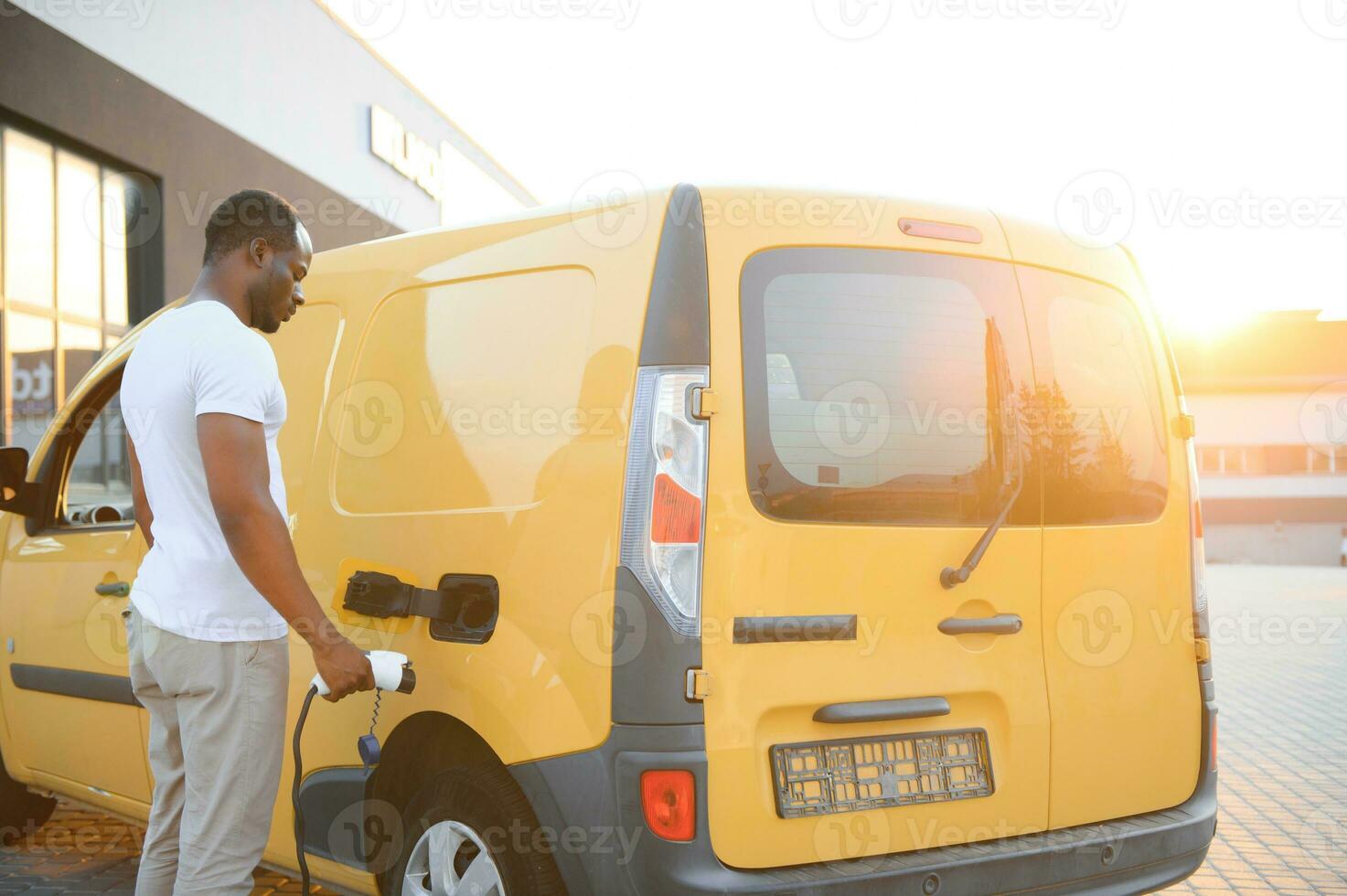 african man holding charge cable in on hand standing near electric car photo