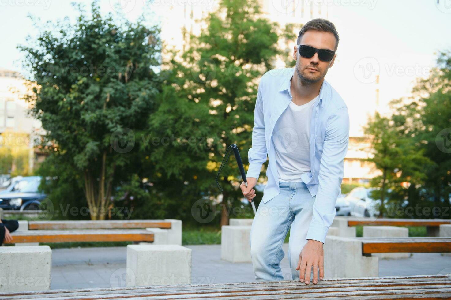 Blind man with a walking stick sitting on a bench at a park photo