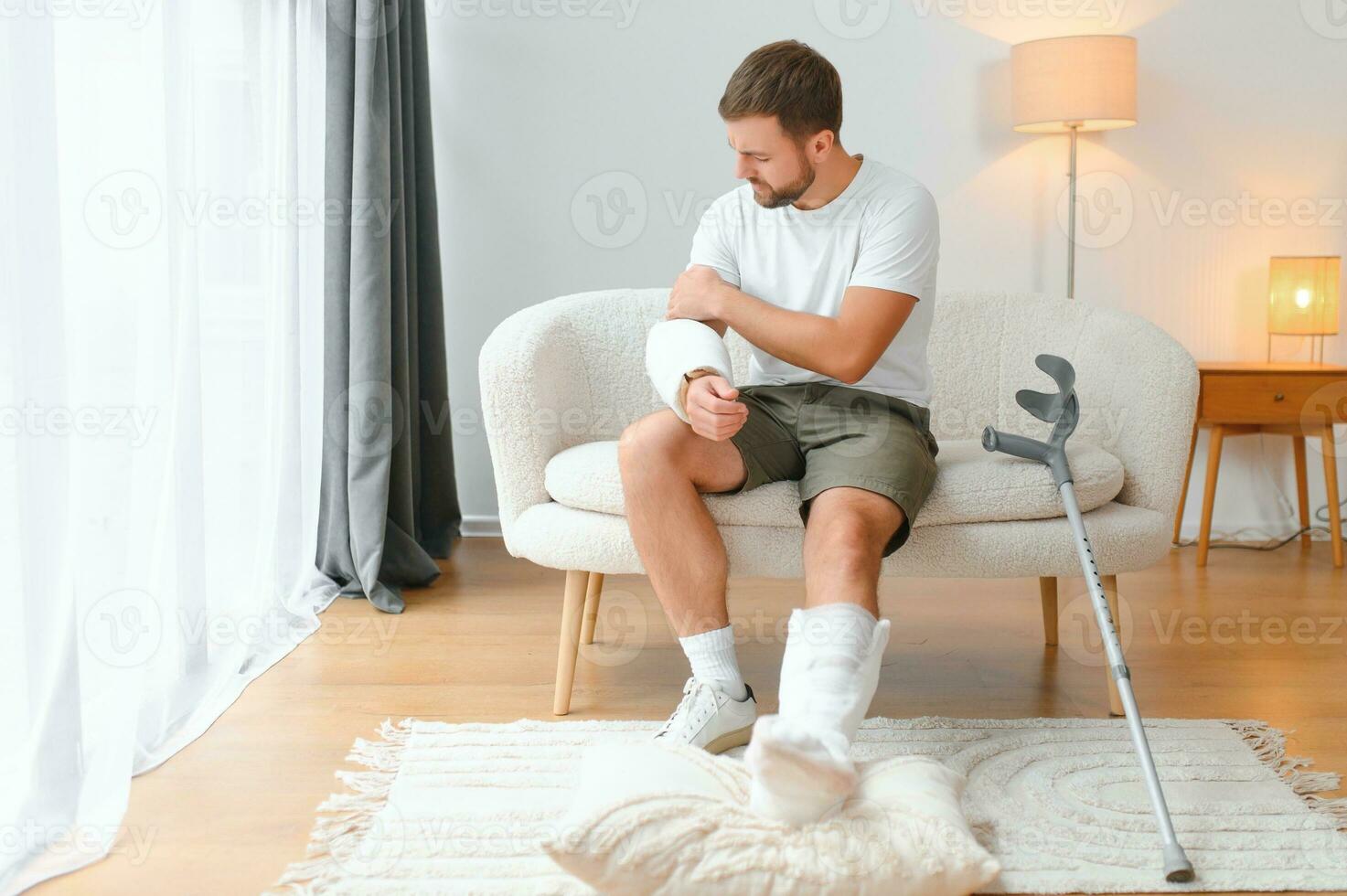 man recovery from accident fracture broken bone injury with leg splints in cast neck splints collar arm splints sling support arm in living room. Social security and health insurance concept photo