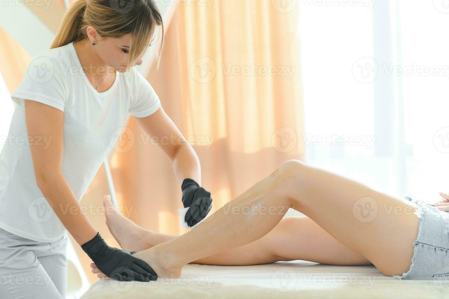 Beautician waxing female legs in spa center photo