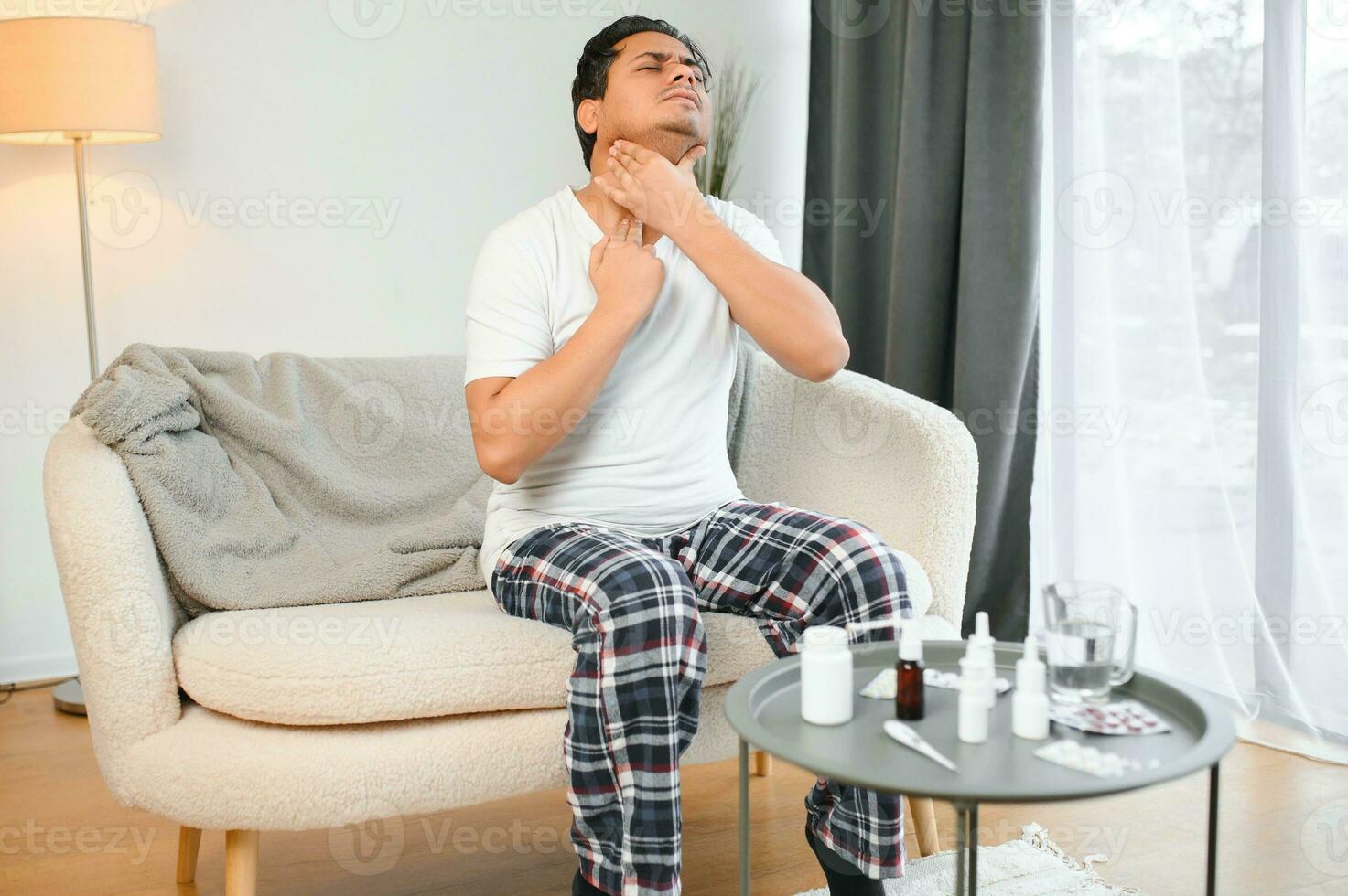 Sick young indian man suffering throat ache while sitting on bed at home photo