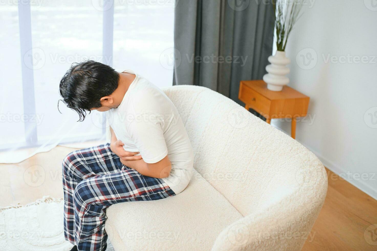 Sad exhausted guy of indian and arabian ethnicity, holds his hands on his stomach, grimaces from pain in his stomach, suffers from poisoning, spasm, stomach problems photo