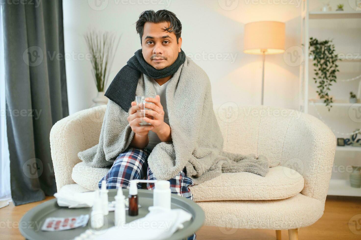 health, cold and people concept - sick young indian man in blanket having headache or fever at home photo