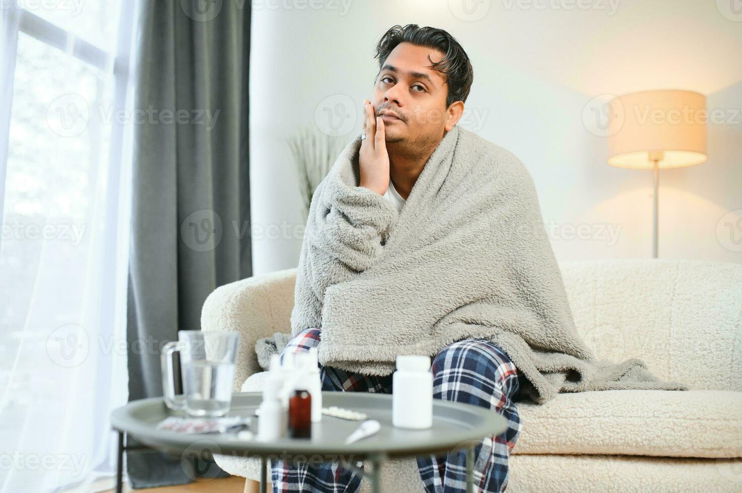 Sick Indian man in plaid sit alone shivering from cold. Unhealthy Arabian guy sit on chair feeling discomfort try to warming up photo