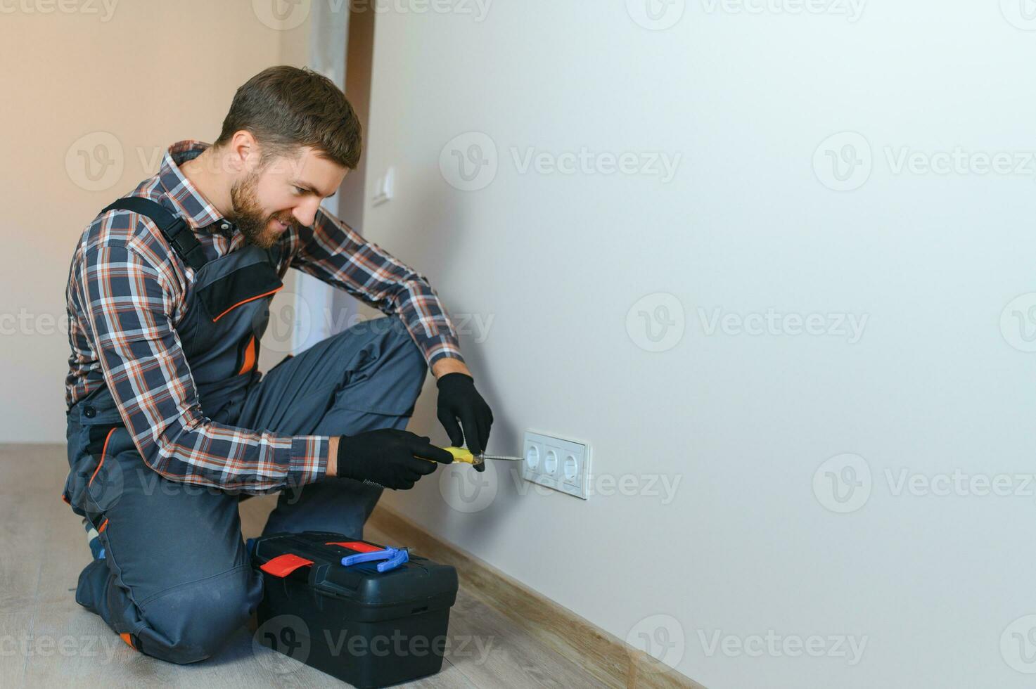 Confident professional electrician in uniform using screwdriver while replacing a socket in apartment after renovation work. photo