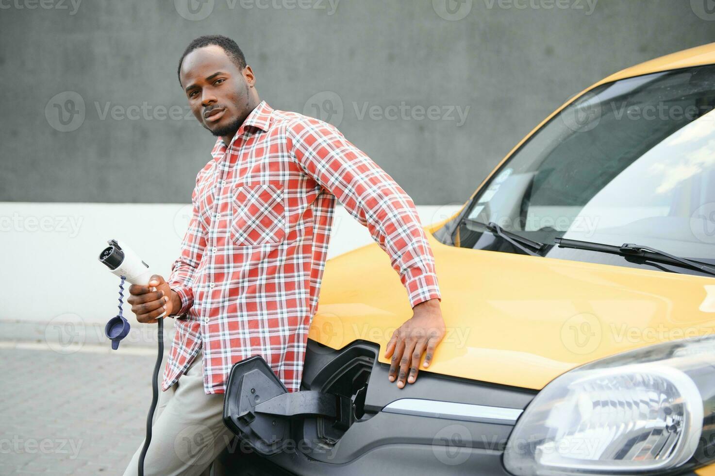 Stylish man inserts the charging cable into the socket of electric car photo